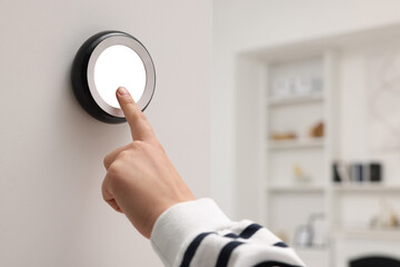 Woman adjusting thermostat on white wall indoors, closeup. Smart home system