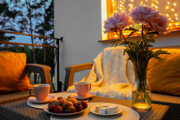 Rattan table with drink, food and flowers on outdoor terrace in evening