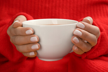 Woman with white polish on nails holding cup of hot drink, closeup