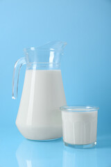 Jug and glass of fresh milk on light blue background