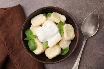 Bowl of tasty lazy dumplings with sour cream and mint leaves on brown table, flat lay