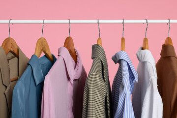 Rack with stylish clothes on wooden hangers against pink background, closeup