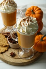 Tasty pumpkin latte with whipped cream in glasses, spices and cookies on white table, closeup