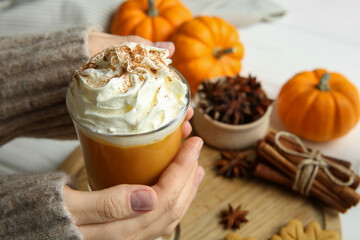 Woman holding cup of tasty pumpkin spice latte with whipped cream at white table, closeup