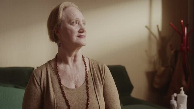 Senior woman with short hair sitting on bed with pensive expression. Cinematic 4k.