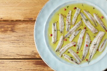 Tasty pickled anchovies with spices on wooden table, top view. Space for text