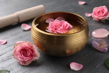 Tibetan singing bowl with water, beautiful rose flowers, mallet and stones on gray table, closeup