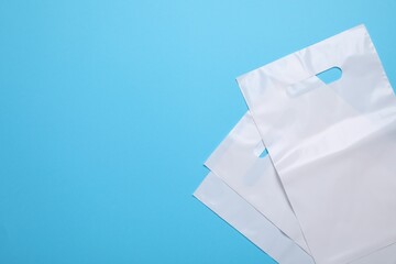 White plastic bags on light blue background, top view. Space for text