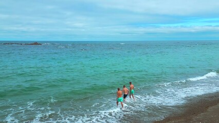 Top view of people running into sea. Clip. Men run to swim in blue sea on background of cloudy horizon. Men run to swim on coast of beautiful sea with reefs