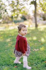 Little girl is standing on the green grass in the garden, looking interestedly to the side