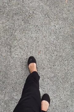 personal perspective looking down with woman wearing black shoes walking on footpath