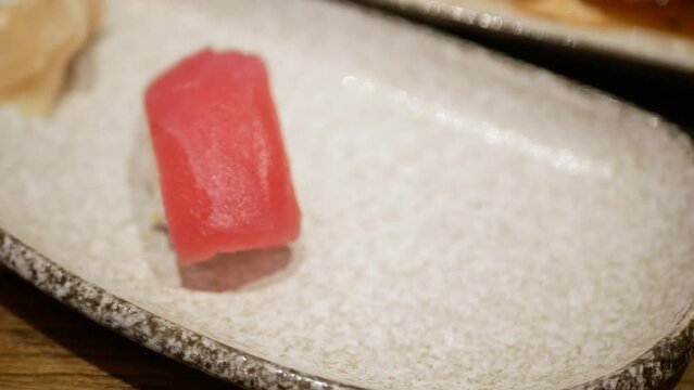 view to a plate of shushi while using chopstick to grab tuna shushi to eat in japanese restaurant, red tuna fish shushi for japanese meal dinner
