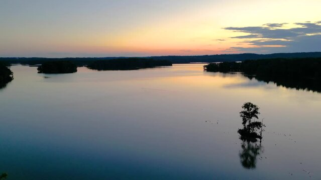 Drone footage over Loch Raven Reservoir with silhouette view of plants on lake shores at sunset, USA