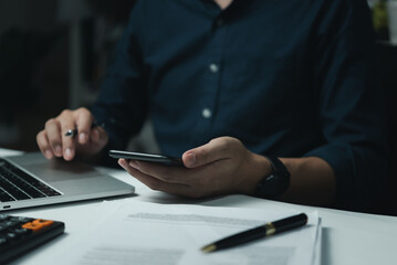 Businessman hand holding mobile smartphone on a table with a laptop at office....