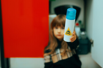 Little Girl Holding a Poisonous Substance from the Detergents Cabinet. Child in danger handling harmful toxic sprays in the kitchen
 - obrazy, fototapety, plakaty