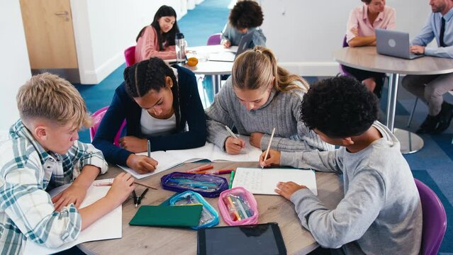 Group of secondary or high school students sitting around table collaborating in study area - shot in slow motion