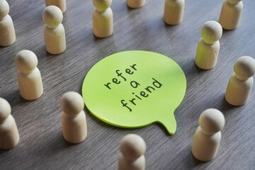 Closeup image of speech bubble with text REFER A FRIEND surrounded by a group of wooden dolls.