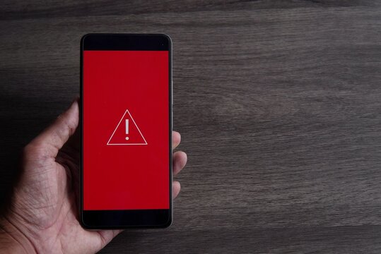 Smartphone with triangle caution warning icon. Copy space for text. System error, malware and cyber crime concept.