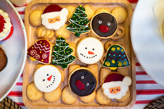 Christmas cookie homemade with sugar icing painted cartoon character of Santa Claus, Pine Tree, Snowman, Jingle Bells and Gingerbread Man on wooden tray for dinner party