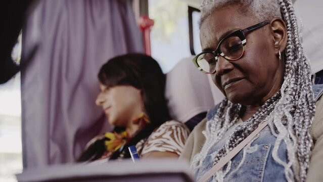 Mulher negra senior com estiloso cabelo afro, fazendo anotacoes em um caderno durante trajeto de onibus. Cinematic 4k.