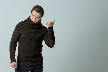 A man on a gray background in a brown sweater showing emotions, shows his hands.