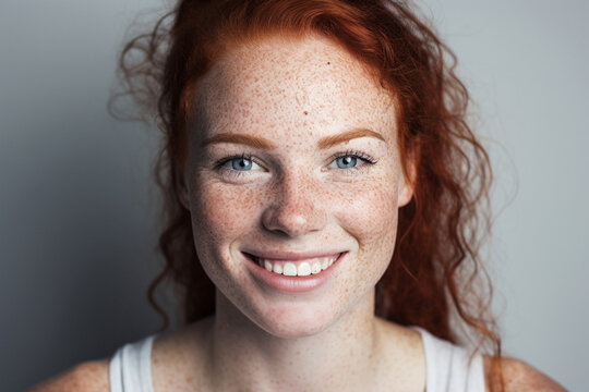 Portrait of a young and beautiful woman with vibrant red hair and natural freckles,The image is bathed in dark red and dusty green tones, creating a unique atmosphere. Generative AI.