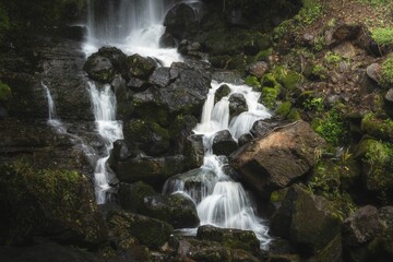 Obraz premium small waterfall with lots of green rocks and grass on the side