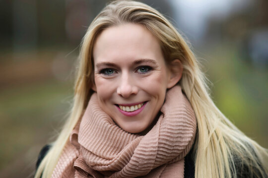 Young woman blonde head portrait landscape format colored, woman with pink scarf in winter clothes smiles into the camera.