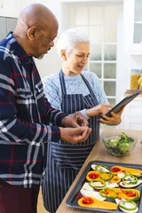  Diverse senior couple preparing healthy meal with vegetables using tablet in kitchen © wavebreak3
