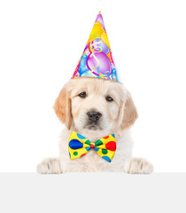 Golden retriever puppy wearing party cap and tie bow looks above empty white banner. isolated on white background
