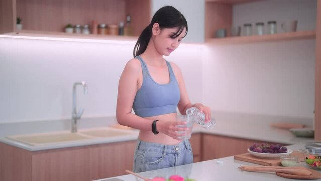 Asian sportswoman in sportswear drinking water in her kitchen at home. She prioritizes maintaining good health, consuming nutritious food, and sustaining a positive body image