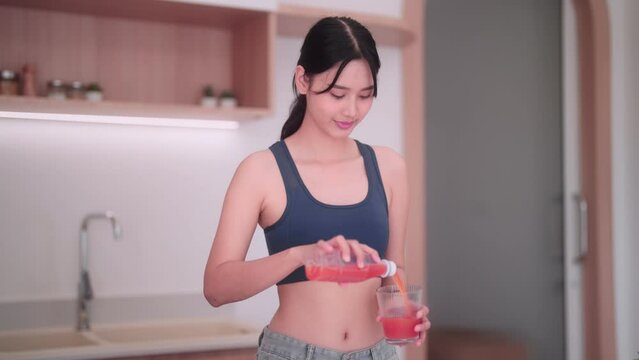 Asian sportswoman in sportswear sipping on a refreshing homemade fruit and vegetable drink in her kitchen. Prioritizing good health, she opts for nutritious food to maintain a positive body image