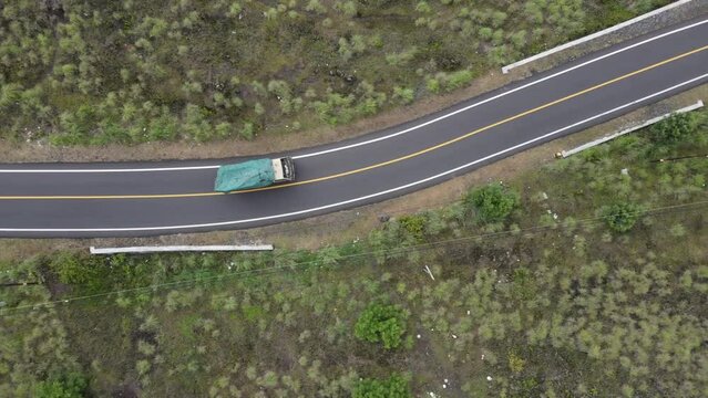 The drone view follows a truck crossing a road carrying a load. Highway that passes through beautiful rice fields