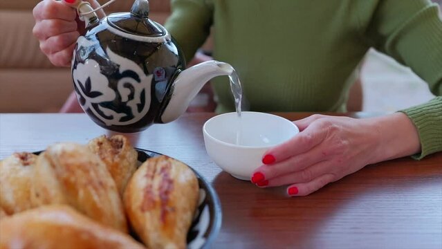 Woman pouring tea from traditional uzbek teapot in cafe