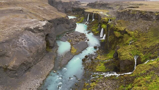 Aerial view of waterfalls flowing into canyon in the Iceland wilderness and rugged terrain.