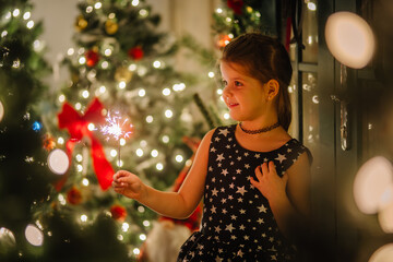 A little girl in a black dress with stars in a Christmas atmosphere. The girl is happy for...