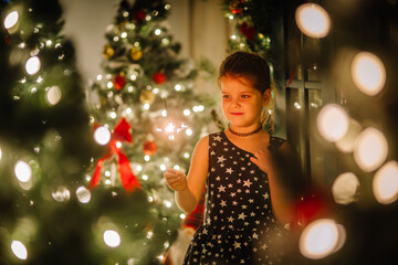 A little girl in a black dress with stars in a Christmas atmosphere. The girl is happy for Christmas. Christmas decorations.