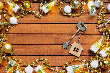 Key to house with a keychain tiny home on wooden background with Christmas decor layout. Gift for New Year, Christmas. Building, project, moving to new house, mortgage, rent and purchase real estate