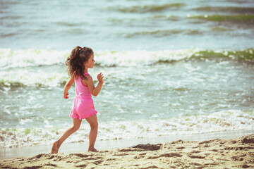 A happy little girl runs on the beach in summer back to the camera