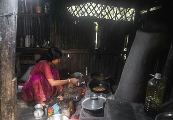South asian young rural housewife cooking in a traditional muddy kitchen 