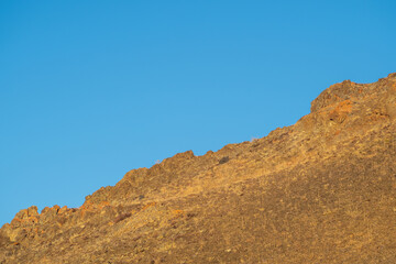 Diagonal red mountain slope against a clear blue sky. View of mountain top and clear blue sky.