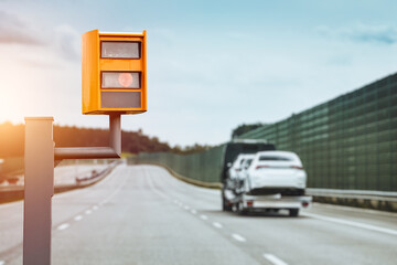 A radar-equipped speed camera monitors the traffic on a road, flashing a yellow light when it catches a car exceeding the speed limit, and using technology to identify the vehicle and enforce the law.