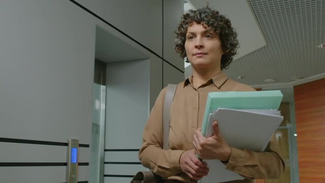 Waist up tracking slowmo shot of Caucasian executive manager carrying paperwork and walking along hallway in modern office