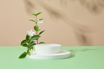 Front view of stack of white round podiums on brown background with green leaves and white flower....