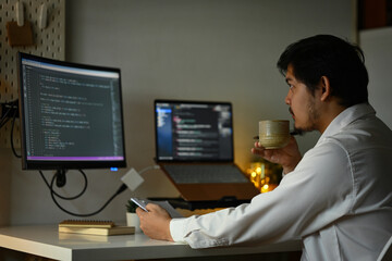 Fototapeta na wymiar Bearded male software developer drinking coffee and coding at home office