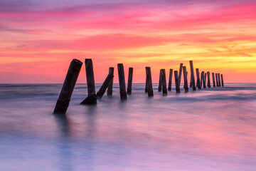 Scenery view of the concrete columns of the old port with Beautiful sky sunrise on Sao Iang Beach at Phetchaburi province. Long exposure picture  - obrazy, fototapety, plakaty