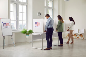 Back view of a group of young American citizens people voters men and women standing in a row at vote center with USA flags in voting booth making a choice on the ballots on election day. - obrazy, fototapety, plakaty