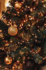 Golden shiny Christmas balls hanging on a Christmas tree with gold garland lights. Decorated spruce...