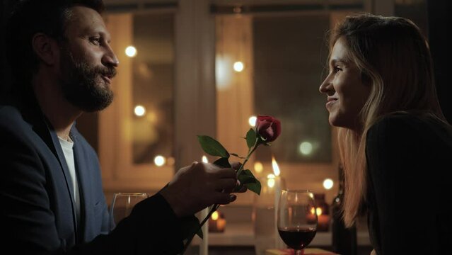 Date, Valentines Day, first date. Man during romantic candlelight dinner in restaurant or at home gives woman one rose