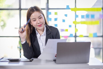 Asian Businesswoman Using laptop computer and working at office with calculator document on desk, doing planning analyzing the financial report, business plan investment, finance analysis concept.
